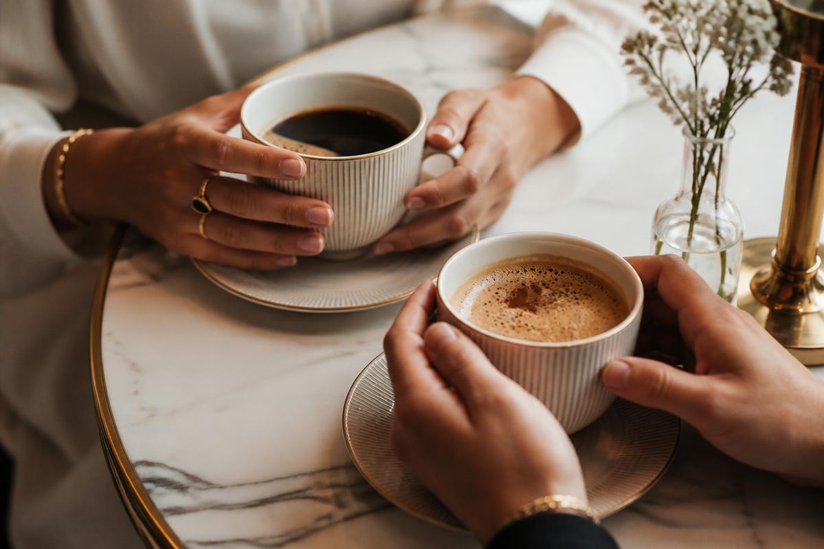Hände halten Kaffeetassen auf Marmortisch